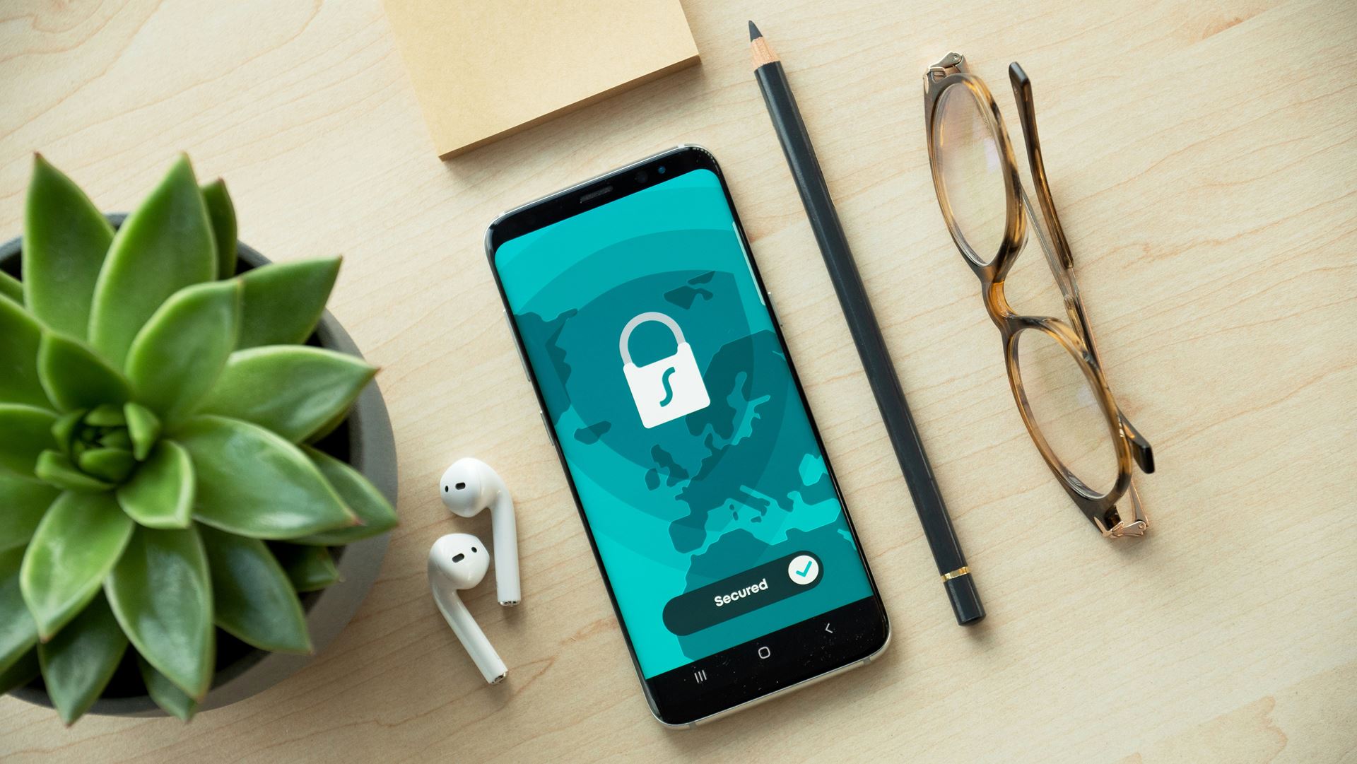 desk with plant ear pods pencil and glasses then a mobile phone with a padlock icon on the screen